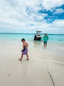 A family enjoys a day at the beach, with children playing in the sand while a boat is anchored nearby — perfect for a fun-filled day on the water.