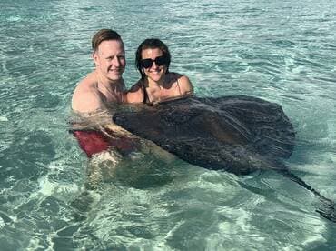 A couple enjoys a memorable experience swimming with a stingray in the clear waters, showcasing a unique wildlife interaction in a tropical paradise.