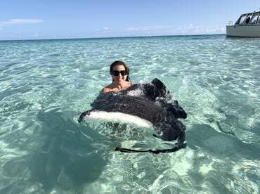 A woman joyfully interacts with a stingray in the crystal-clear waters, showcasing a unique wildlife experience in a tropical paradise.