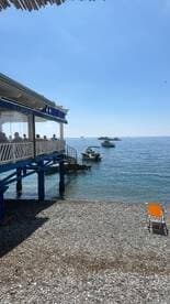 A picturesque view of a beachside restaurant with patrons enjoying the scenery, featuring boats anchored in the calm waters — a perfect spot for relaxation and dining by the sea.