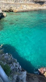 A stunning view of crystal-clear waters along a rocky coastline, with people enjoying the sun and swimming — a perfect destination for beach lovers.
