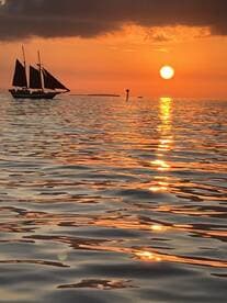 A stunning sunset view featuring a sailboat gracefully gliding across the water, reflecting the vibrant colors of the sky — perfect for capturing the essence of serene evening cruises.