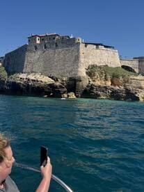 A guest captures a stunning view of a historic fortress from a boat, showcasing the beautiful coastline and clear blue waters.