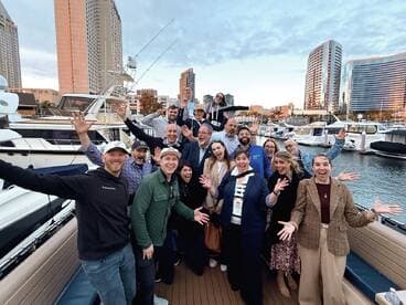 A lively group of guests celebrates aboard a boat, showcasing camaraderie and joy in a vibrant marina setting.