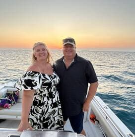 A joyful couple poses for a photo on their boat at sunset, capturing a perfect moment for romantic getaways or special celebrations on the water.