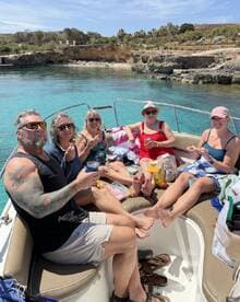 A lively group enjoys snacks and drinks aboard a boat, soaking up the sun and good company in a picturesque setting.