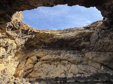 A stunning view of a natural cave formation with a clear blue sky above, showcasing the beauty of coastal landscapes — perfect for adventure seekers exploring hidden gems.