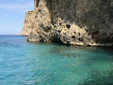 A stunning view of rugged cliffs meeting crystal-clear turquoise waters, showcasing the natural beauty of the coastline — perfect for eco tours or scenic boat trips.