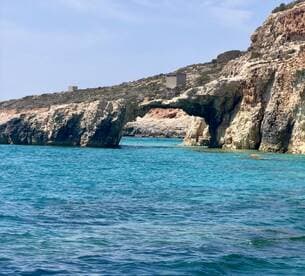 A stunning view of a natural rock arch along the coastline, surrounded by crystal-clear turquoise waters — a perfect destination for boat tours and sightseeing.