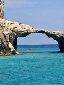 A stunning view of a natural rock arch over crystal-clear turquoise waters, showcasing the beauty of coastal landscapes — perfect for island hopping adventures.