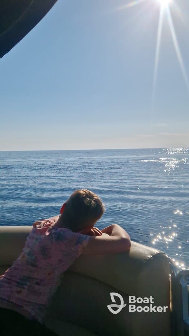 A young person relaxes on the boat, gazing out at the serene ocean under a bright sun — a perfect moment of tranquility on the water.