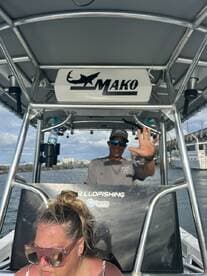 A friendly captain waves from the helm of a Mako boat, showcasing the excitement of a fishing adventure on the water.