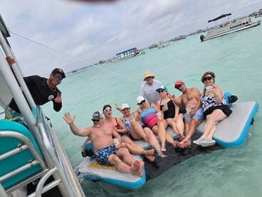 A lively group enjoys a fun day on a floating mat in the turquoise waters, complete with cocktails and smiles, perfect for a memorable beach outing.