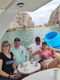 A cheerful group enjoys drinks on a boat with a stunning beach backdrop, perfect for a fun day out on the water.