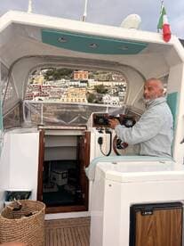 A captain navigates from the helm of a well-equipped boat, showcasing the cozy interior and stunning coastal views in the background.