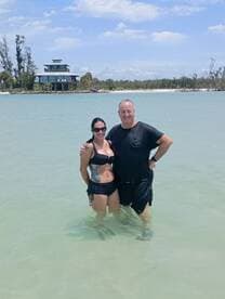 A couple enjoys a sunny day at the beach, standing in shallow water with a beautiful backdrop — perfect for romantic getaways or beach vacations.