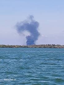An unclear image showing smoke rising in the distance over water, possibly indicating a fire or other incident.