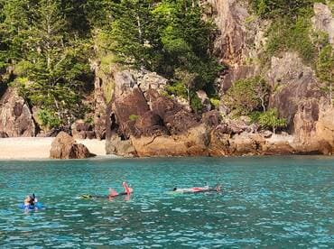 Two snorkelers explore the vibrant waters near a rocky coastline, enjoying a perfect day of swimming and adventure at the beach.