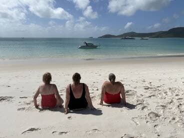 Three friends relax on the beach, enjoying the serene ocean view with a boat in the distance — a perfect getaway for sun and relaxation.