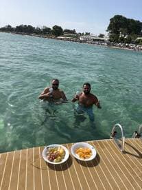 Two friends enjoy a refreshing swim in crystal-clear waters while celebrating with snacks on a sunny beach day — a perfect moment for relaxation and fun.
