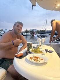 A man enjoys snacks and drinks on a boat, surrounded by a picturesque marina setting — perfect for relaxing moments on the water.
