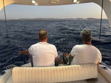 Two men enjoy a serene moment on the deck of a boat, gazing at the ocean scenery — a perfect setting for relaxation and connection with nature.
