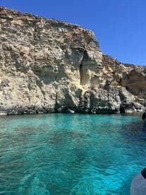 A stunning view of a rocky coastline with crystal-clear waters, where swimmers enjoy the refreshing sea — a perfect destination for a summer adventure.