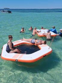 A lively group enjoys a fun day in the water on a floating mat, surrounded by clear turquoise waters — perfect for summer parties and relaxation.