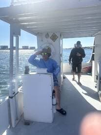 Two individuals are seen aboard a boat, with one at the helm and the other walking around, showcasing a relaxed day on the water.
