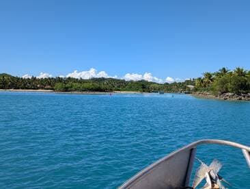 A scenic view from the bow of a boat navigating through clear turquoise waters, surrounded by lush greenery and sandy beaches — perfect for exploring tropical destinations.