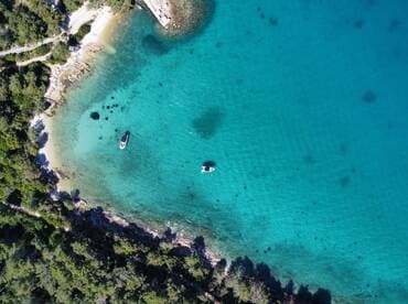 Aerial view of boats anchored in crystal-clear turquoise waters, surrounded by lush greenery — a perfect scene for exploring hidden coves and enjoying nature.