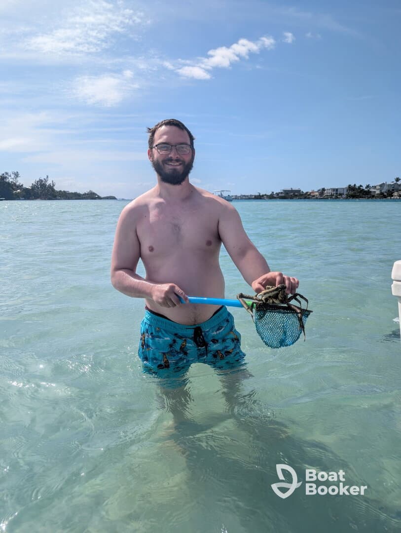 A man enjoys a day in the water, proudly holding a crab caught with a net — a perfect snapshot of outdoor adventure and fishing fun.