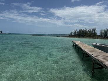 A scenic view of a wooden dock extending into clear turquoise waters, surrounded by lush greenery — a tranquil spot ideal for boating adventures.