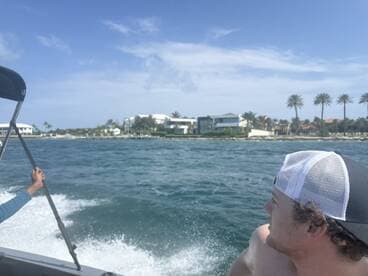 A scenic view from a boat with passengers enjoying the ride, showcasing beautiful waterfront homes and palm trees along the coastline.