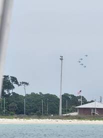 An unclear image featuring jets flying in formation above a coastal area, with limited visibility of the boat or surrounding scenery.