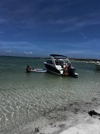 A group enjoys a sunny day at the beach, swimming and relaxing near their boat — a perfect setting for summer fun and water activities.