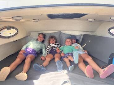 A cozy cabin space on a boat features four children relaxing on a comfortable bed, showcasing the perfect spot for family fun and relaxation while on the water.
