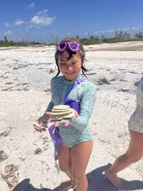 A young girl proudly displays her collection of shells on the beach, capturing the joy of a fun day in nature.