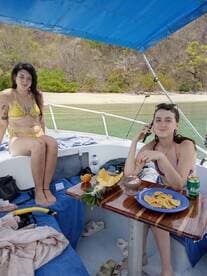 Two friends enjoy snacks and drinks on a boat, surrounded by beautiful beach scenery — a perfect moment of relaxation on the water.