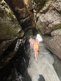 Two friends explore a stunning cave while wading through shallow water, showcasing the beauty of nature and adventure on their trip.