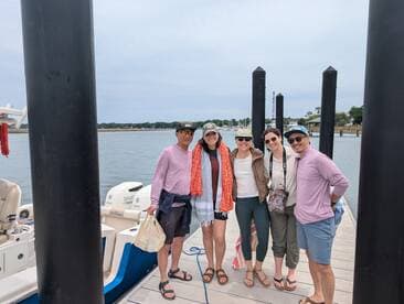 A cheerful group of friends poses together on the dock beside a boat, ready for a fun day on the water.