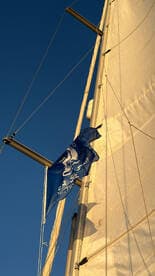 Close-up view of a sail and flag on a sailing vessel against a clear blue sky, showcasing the elegance of sailing.