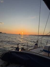 A serene sunset view from the deck of a sailboat, showcasing the tranquil waters and distant horizon — perfect for evening cruises.