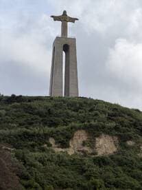 A view of the Christ the Redeemer statue on a hill, surrounded by lush greenery and cloudy skies. This iconic landmark is a popular destination for tourists.