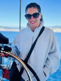 A woman stands at the helm of a boat, showcasing the interior space while enjoying a sunny day on the water.