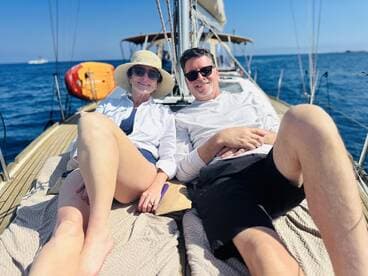 A couple enjoys a relaxing moment on the deck of a sailboat, soaking up the sun and the beautiful ocean views — perfect for a romantic getaway.