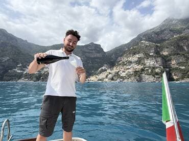 A man pours champagne while enjoying the stunning coastal views from a boat, capturing the essence of celebration on the water.