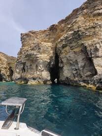 A stunning view of rocky cliffs and a natural cave entrance, captured from a boat in crystal-clear waters — perfect for exploring coastal wonders.