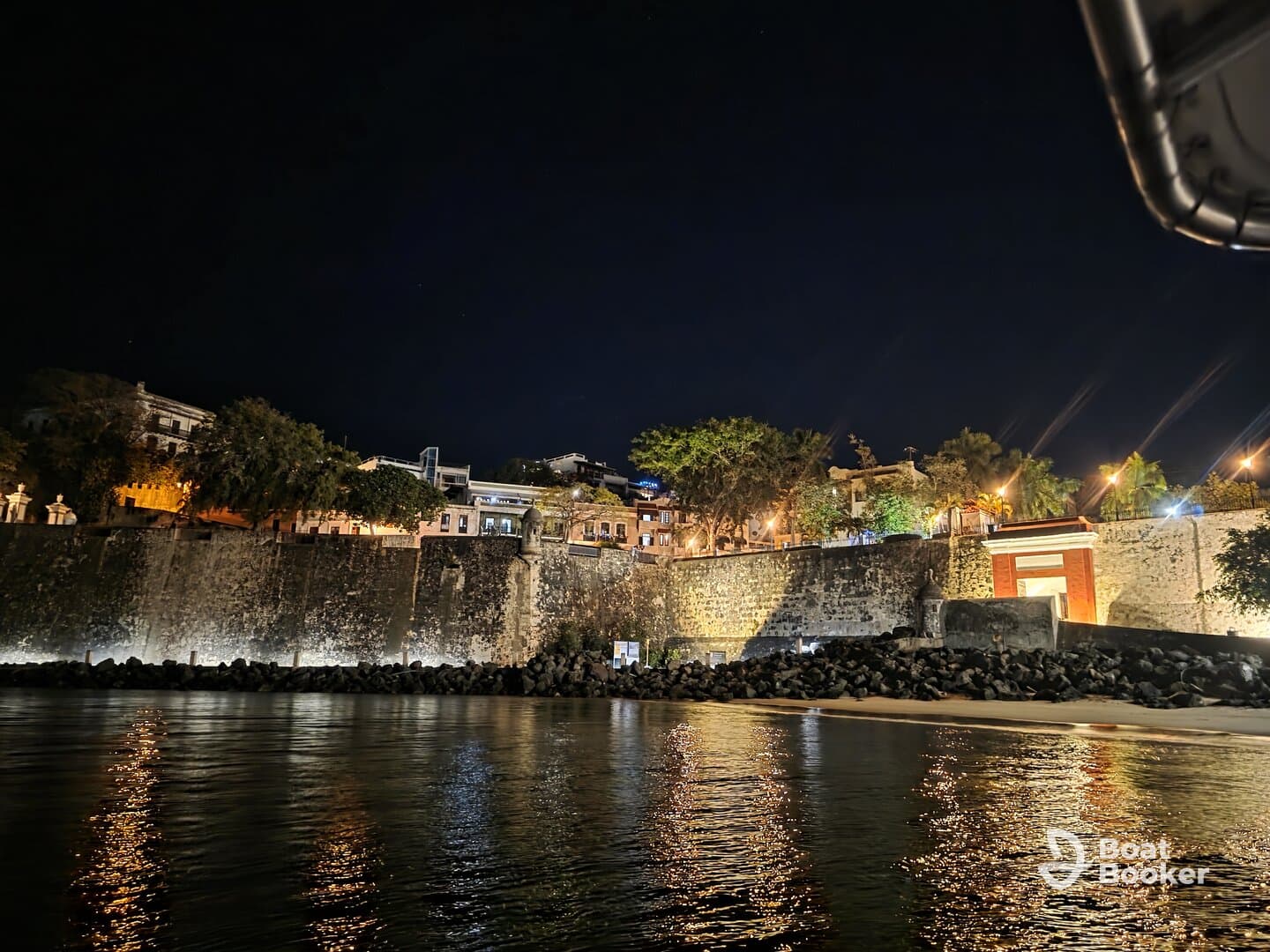 A nighttime view of a waterfront scene with illuminated buildings and a rocky shoreline, creating a serene atmosphere.