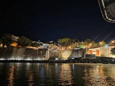 A nighttime view of a waterfront scene with illuminated buildings and a rocky shoreline, creating a serene atmosphere.